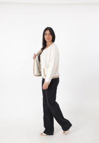 Cardigan in maglia crema con accenti beige, scollatura rotonda, chiusure a bottoni e tasche frontali, abbinato a jeans neri a zampa d'elefante e scarpe con punta aperta.