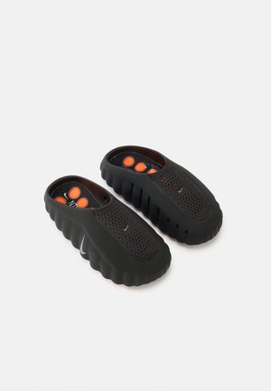 Juodi, gumine medžiaga pagaminti slip-on tipo batai su tekstūruotu viršumi, ventiliacijai skirtomis perforacijomis ir minkštu vidumi su oranžiniais akcentais.