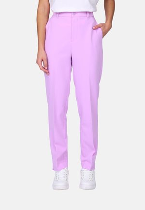 Femme portant un pantalon lavande taille haute à coupe droite avec des poches latérales et des baskets blanches, debout devant un fond uni.