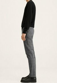Zwarte blouse met lange mouwen gecombineerd met grijze geruite broeken en zwarte laarzen. De outfit heeft een ontspannen pasvorm en soepele texturen.
