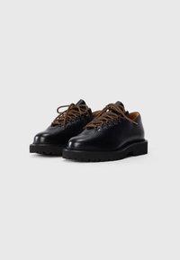 Black leather shoes with a textured finish, brown laces, and a thick black sole. Rounded toe and casual design.