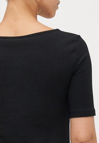 Top nero a maniche corte con scollatura ampia e texture liscia. Presenta una vestibilità aderente e cuciture pulite lungo i bordi.