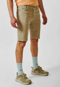 Beige, knielange shorts met een rechte pasvorm, gemaakt van gladde stof. Draagt mintgroene sokken en beige sneakers.