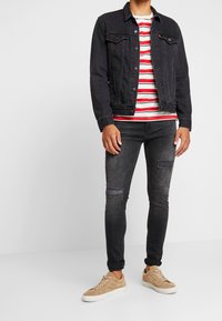 Chaqueta de mezclilla negra sobre una camiseta de rayas rojas y blancas, combinada con jeans oscuros desgastados y zapatillas de tono claro.