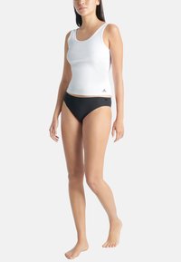 Vit ribbad tanktop med rund halsringning, matchad med svarta bikiniunderdelar med en liten logotyp. Båda är tillverkade av stretchigt tyg.