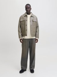 Graue Lederjacke mit zwei Fronttaschen, kombiniert mit einem cremefarbenen Strickpullover und lockeren grauen Jeans, dazu schwarze Schuhe.