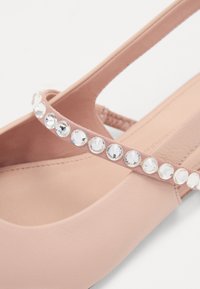 Pink flat shoe with a smooth texture, featuring a slim strap adorned with clear rhinestones along the edge. Simple design, rounded toe.
