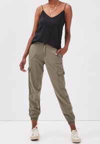 Black camisole top with spaghetti straps, olive green cargo pants featuring side pockets, and beige sneakers. Casual fit, soft fabric.