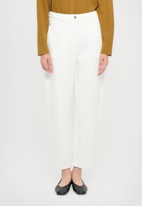 Pantaloni bianchi su misura con design a gamba dritta, dotati di tasche anteriori e chiusura con bottone. Abbinati a una camicia marrone a maniche lunghe.