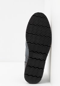 Sneaker en cuir gris avec une semelle en caoutchouc noir texturé présentant des motifs en zigzag. Détails de couture et accent latéral visibles. Taille indiquée comme 37.