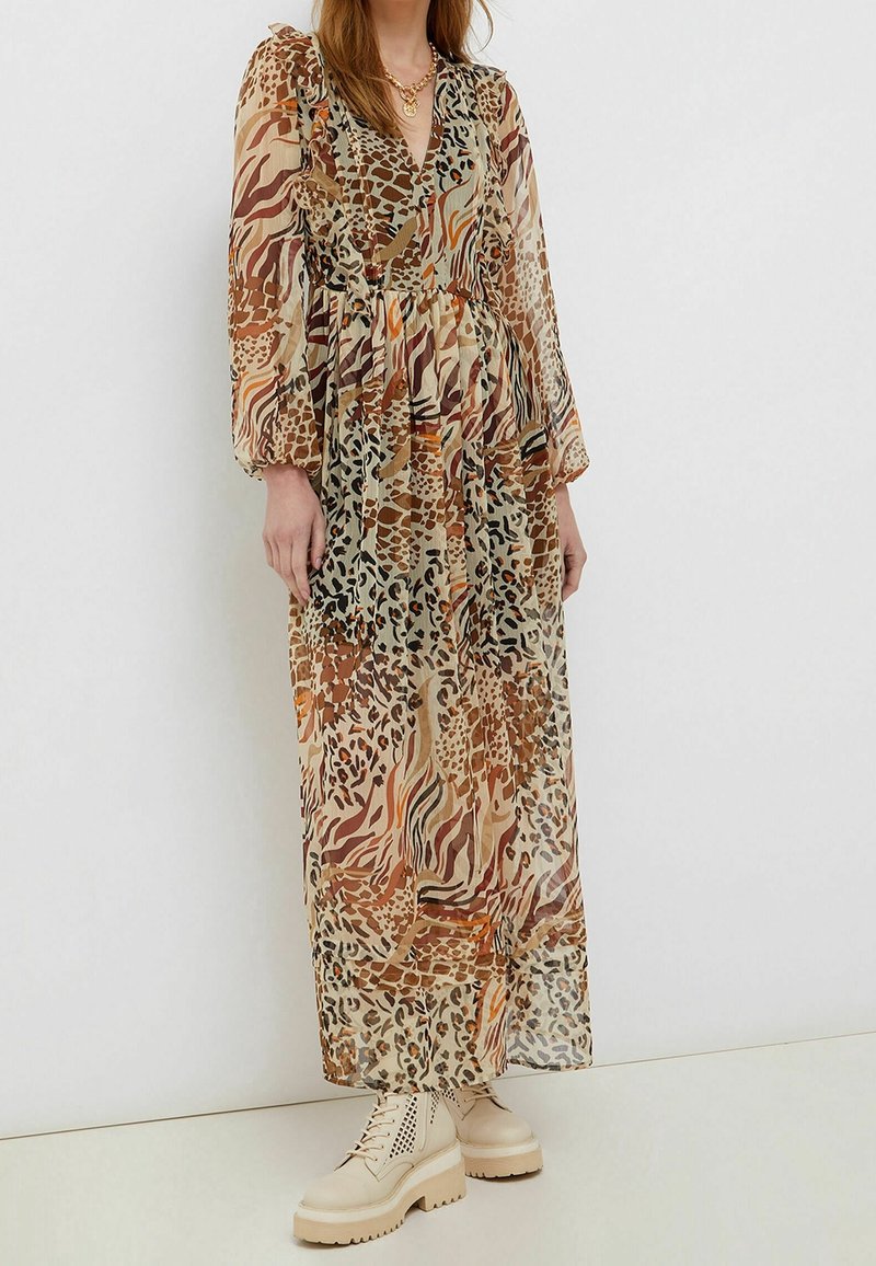 Femme portant une longue robe transparente à imprimé animal marron et beige, associée à des bottines épaisses crème à lacets.