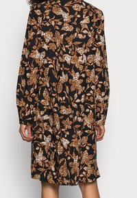 Svart klänning med långa ärmar, prydd med blommönster och leopardtryck i orange och vitt. Lätt lös passform med knappar vid ärmsluten.