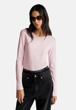 Frau mit Schildpatt-Sonnenbrille, einem hellrosa Langarmshirt und schwarzen hoch geschnittenen Jeans mit elastischem, markiertem Bund.