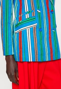 Multicolor gestreepte blazer in blauw, groen, rood en bruin met witte accenten. Voorzien van een dubbelzijdig ontwerp en klepzakken.
