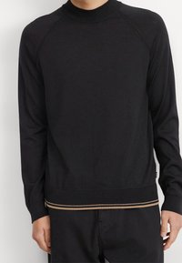 Czarny sweter z długim rękawem i okrągłym dekoltem, ze ściągaczami na mankietach i na dole. Posiada kontrastowy beżowy pasek przy dolnej krawędzi. Wykonany z miękkiego materiału.