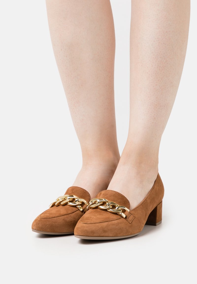 Chaussures à talons carrés en daim camel avec une chaîne dorée en accent sur le devant. Bout arrondi et texture lisse, adaptées à diverses occasions.