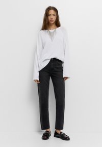 Witte longsleeve top met een gestructureerd ontwerp en zwarte high-waisted jeans. Zwarte instapschoenen met glanzende accenten maken de outfit compleet.