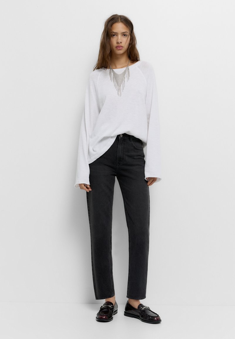 Witte longsleeve top met een gestructureerd ontwerp en zwarte high-waisted jeans. Zwarte instapschoenen met glanzende accenten maken de outfit compleet.