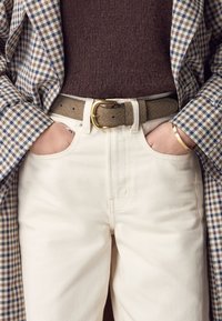 Beige cotton trousers with a smooth texture, paired with a gray-brown textured leather belt featuring a gold buckle and wearing a checkered blazer.