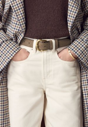 Pantaloni di cotone beige con una texture liscia, abbinati a una cintura in pelle grigio-marrone con fibbia dorata e indossando un blazer a quadri.