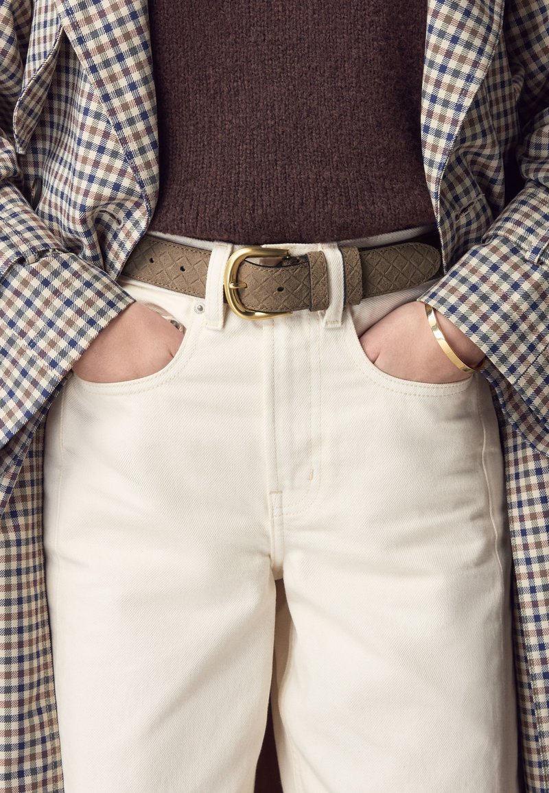 Beige cotton trousers with a smooth texture, paired with a gray-brown textured leather belt featuring a gold buckle and wearing a checkered blazer.