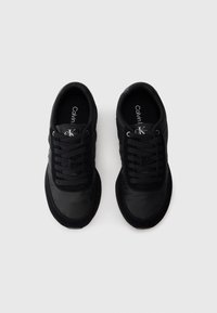 Zwarte sneakers met een gladde bovenkant van stof, vetersluiting, logo op de tong en textuuraccenten aan de zijkant. Het bovenwerk heeft een mix van matte en glanzende afwerkingen.