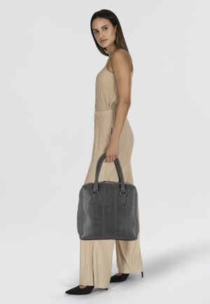 Sac à main en cuir gris avec des motifs en relief, anses doubles et fermeture éclair, associé à une combinaison plissée beige et des talons noirs.