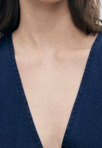 Navyblaues V-Ausschnitt-Gewand mit tiefem Ausschnitt und glatter Textur, sichtbaren Nähten entlang der Kanten und passgenauer Form.