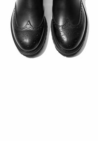Zapatos de cuero negro con un diseño de brogue, decorados con perforaciones, punta redondeada y una suela texturizada y gruesa.