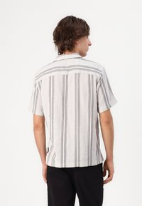 Camisa de manga corta en un tejido texturizado de color gris claro, con rayas verticales negras. La vista trasera muestra un corte relajado y un diseño de cuello.