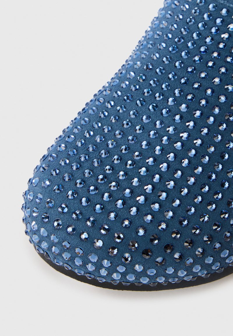 Blauwe suède schoen met een oppervlakte versierd met talloze facetgewonden rhinestones, die een gestructureerd en reflecterend effect creëren.