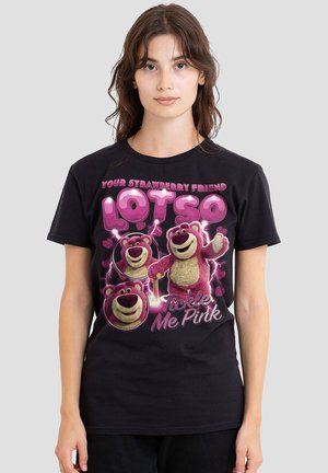 Young woman wearing a black T-shirt featuring pink cartoon bear characters and text "Your Strawberry Friend Lotso, Tickle Me Pink."