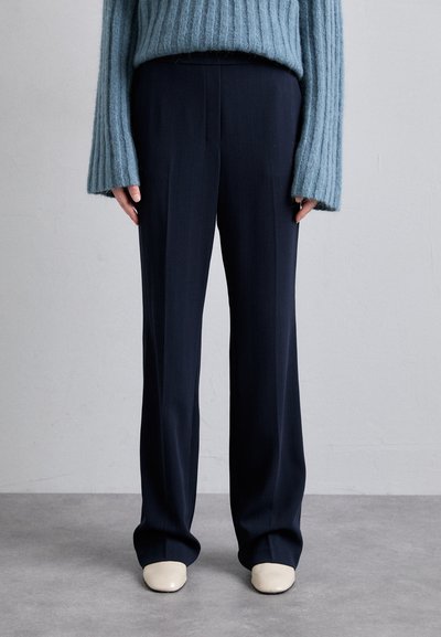 Pantalons tailleurs bleu marine avec une coupe droite, tissu texturé et fines rayures, associés à un pull côtelé bleu clair et des chaussures crème.