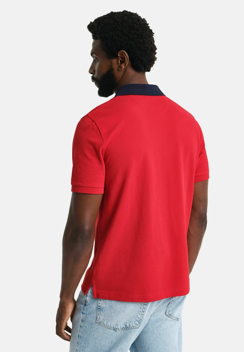 Rotes Poloshirt mit marineblauem Kragen, kurzen Ärmeln und seitlichen Schlitzen; glattes Material mit einfarbigem Design.
