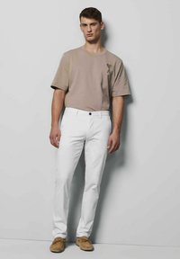 Beige katoenen T-shirt met een hart en de letter "A" grafisch ontwerp, gecombineerd met witte katoenen broek en lichtbruine suède schoenen.