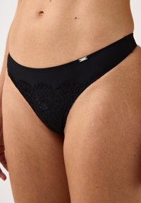 Sort bikini bund med blomsterlæs detaljer foran, glat stof og en tynd talje med en lille mærket metalaccent.