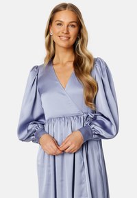 Robe mauve clair avec un design enroulé, de longues manches bouffantes et une taille froncée. Texture lisse avec un léger éclat.