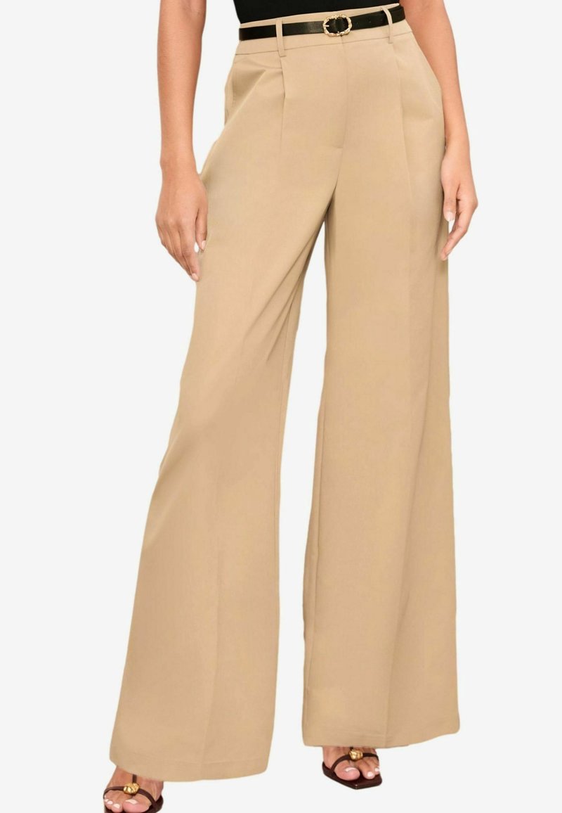 Pantalon beige à jambes larges avec plis à l'avant, porté avec une ceinture noire ornée d'une boucle dorée, assorti à des sandales noires à bouts ouverts.