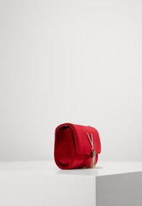 Borsa in camoscio rosso con forma strutturata, chiusura a pattina piatta, dettagli in metallo argentato e catena decorativa. Design semplice e compatto.