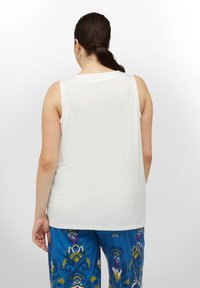 Biała top bez rękawów o gładkiej fakturze. Modelka nosi wzorzyste niebieskie spodnie w kwiatowe i abstrakcyjne wzory.