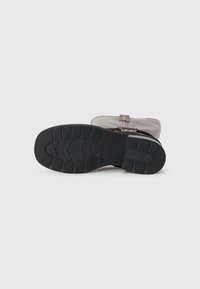 Stivale alla caviglia in tessuto grigio con suola in gomma nera, caratterizzato da motivi testurizzati e una fascia decorativa con accenti metallici.