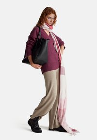 Černá strukturovaná kabelka, fialový pletený svetr s výstřihem do V, světle béžové kalhoty s širokými nohavicemi a růžový pruhovaný šátek s třásněmi.