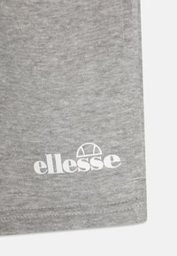 Pelēka kokvilnas auduma ar gludu tekstūru, uz kā redzams balts drukāts logo "ellesse" un apļa dizains virs tā.