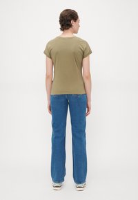 Olivengrønn bomulls t-skjorte med oppbrettede ermer, sammen med lyseblå flagrende jeans. Enkelt design, minimale detaljer, rene linjer.