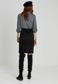 Svart mockapennkjol med hög midja, tillsammans med en grå skjorta med ett litet prickmönster. Höga svarta slouchy stövlar fulländar looken.