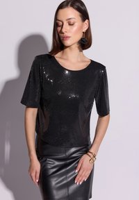 Czarna bluzka z cekinami, krótki rękaw, okrągły dekolt i dopasowana sylwetka, zestawiona ze skórzaną ołówkową spódnicą i złotymi bransoletkami.