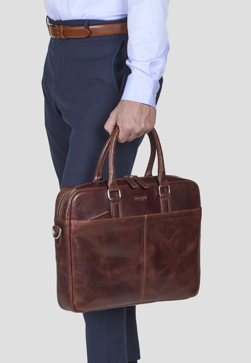 Brun læder arbejdstaske med to håndtag, lynlåslukning på toppen og en frontlomme. Glat tekstur og markante syning detaljer.