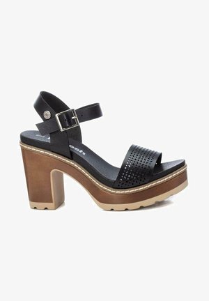 Sandal con tacco nero, realizzato con un upper perforato, cinghia alla caviglia e suola platform marrone chunky. Presenta una fibbia metallica e dettagli cuciti.