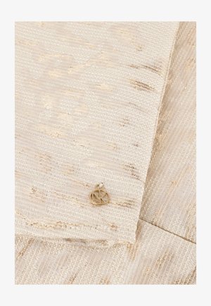 Beige gestructureerde stof met metallic gouden draadjes, met een klein circulair gouden embleem bij de vouw. Glad en verfijnd afwerking.