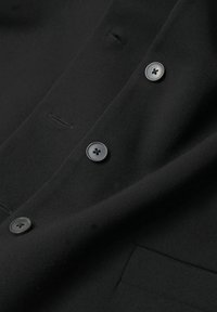 Schwarzes Stoffhemd mit glatter Textur, klassischem Kragen und vier runden schwarzen Knöpfen auf der Vorderseite. Enthält ein kleines Taschen-Detail.